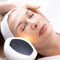 Hand of beautician using laser handle on mature womens face while making laser skin resurfacing, above view